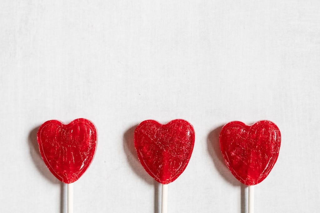 Three red heart-shaped lollipops arranged against a white background, offering a sweet and romantic theme.